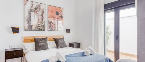 Un dormitorio moderno con cabecera de madera, una cama grande con manta azul, dos mesitas de noche y un ventanal con vistas a zonas verdes.