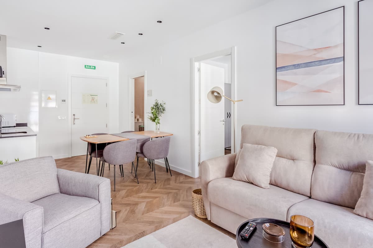 Ein modernes Wohnzimmer mit einer Couch, einem Couchtisch mit Fernbedienung und Glas, sowie einem Essbereich mit Stühlen und Tisch.
