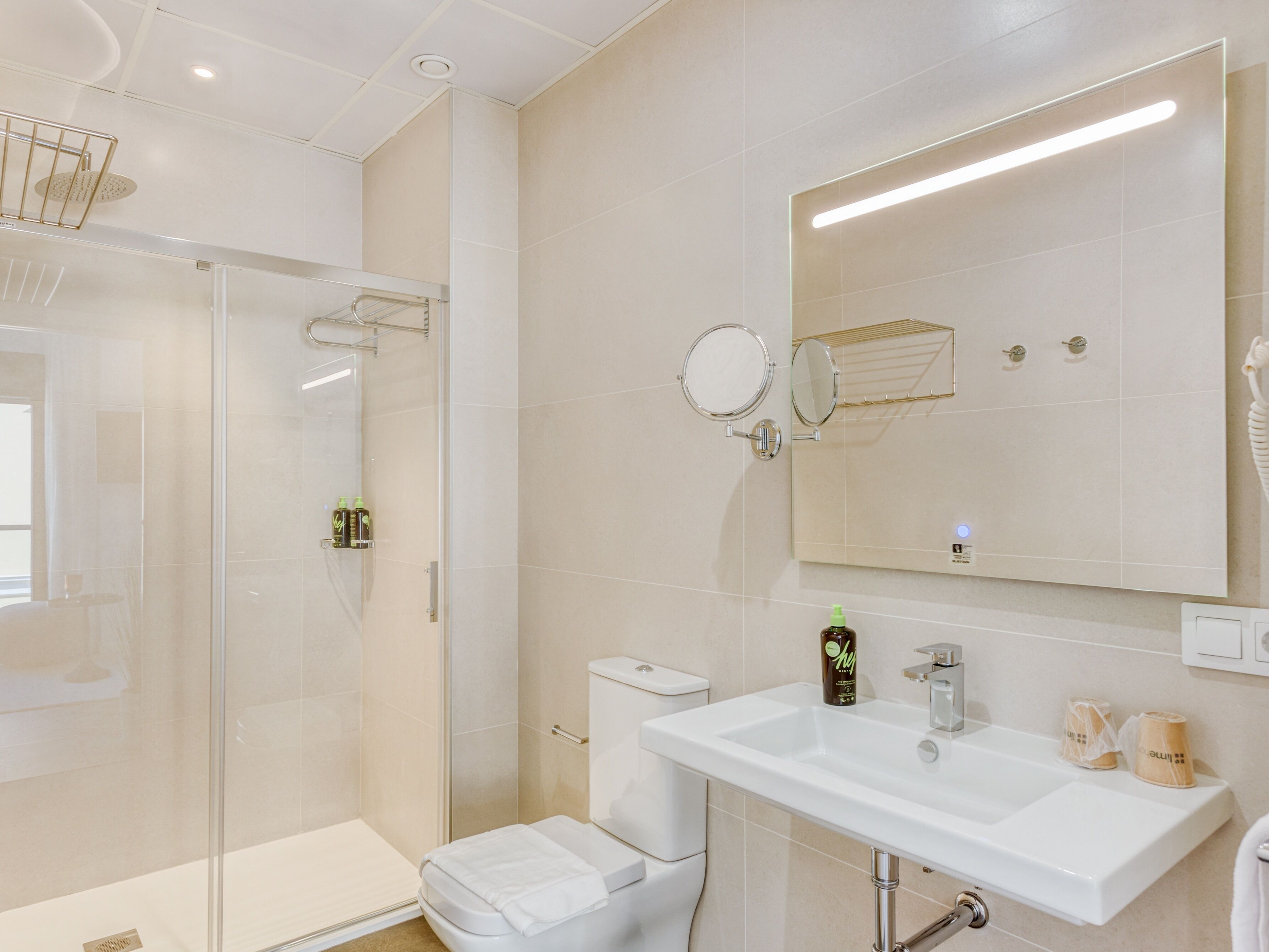 Un baño moderno con cabina de ducha de vidrio, un lavabo blanco y un espejo grande.
