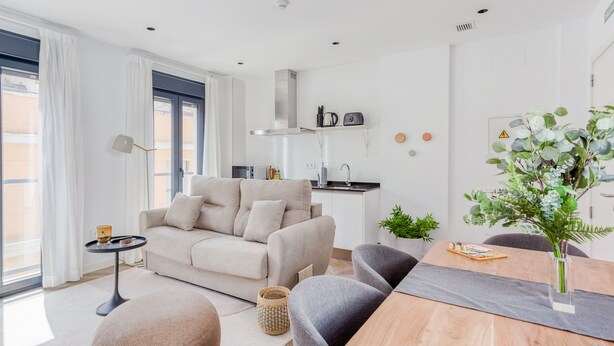 Una sala de estar moderna con un sofá, una mesa de comedor con sillas, una mesita auxiliar y un ventanal con cortinas.