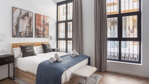 Un dormitorio moderno con una cama grande, un banco y dos ventanas con cortinas.