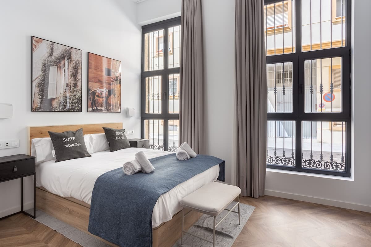 Ein modernes Schlafzimmer mit einem großen Bett, einer Bank und zwei mit Vorhängen versehenen Fenstern.