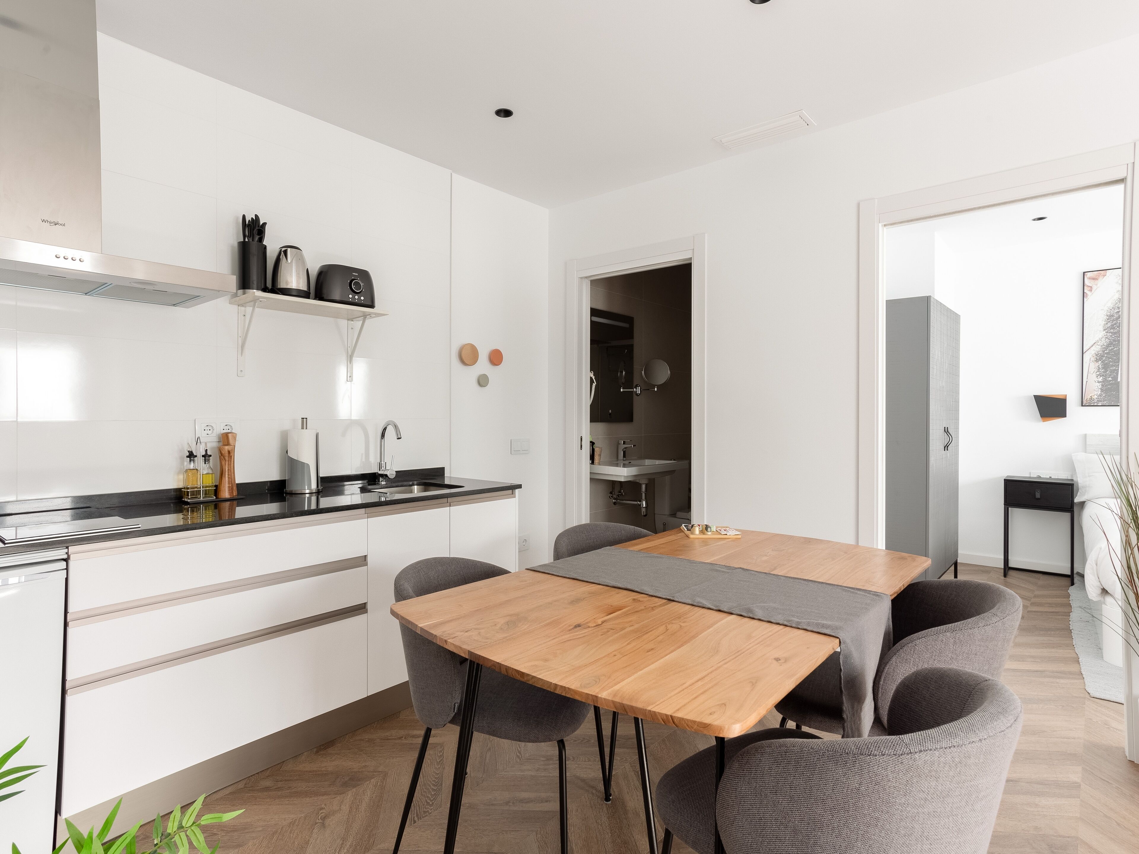 Une cuisine moderne avec des meubles blancs, une table à manger en bois et un canapé gris.