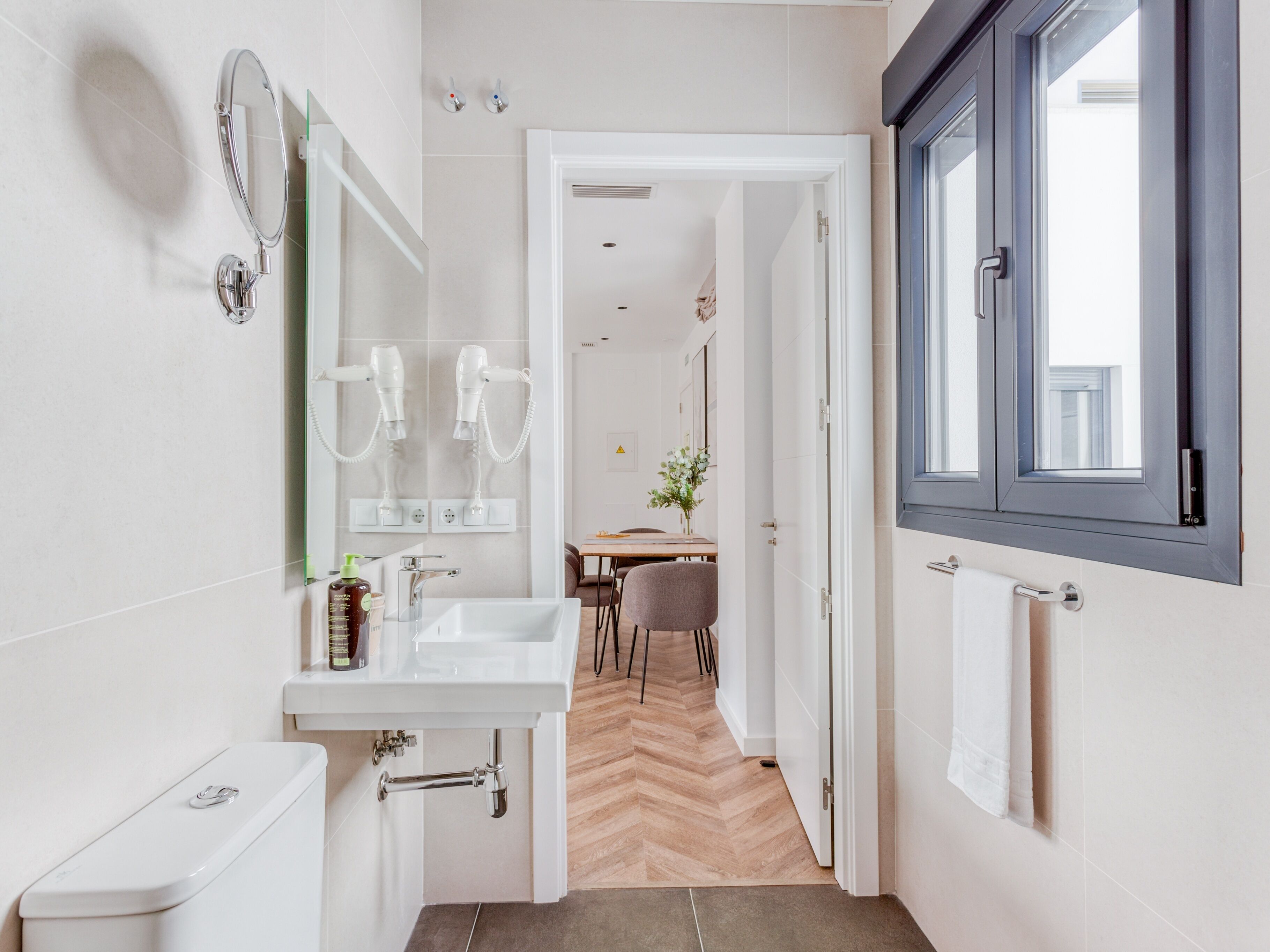 A modern bathroom with a toilet, sink, and two hair dryers mounted on the wall.