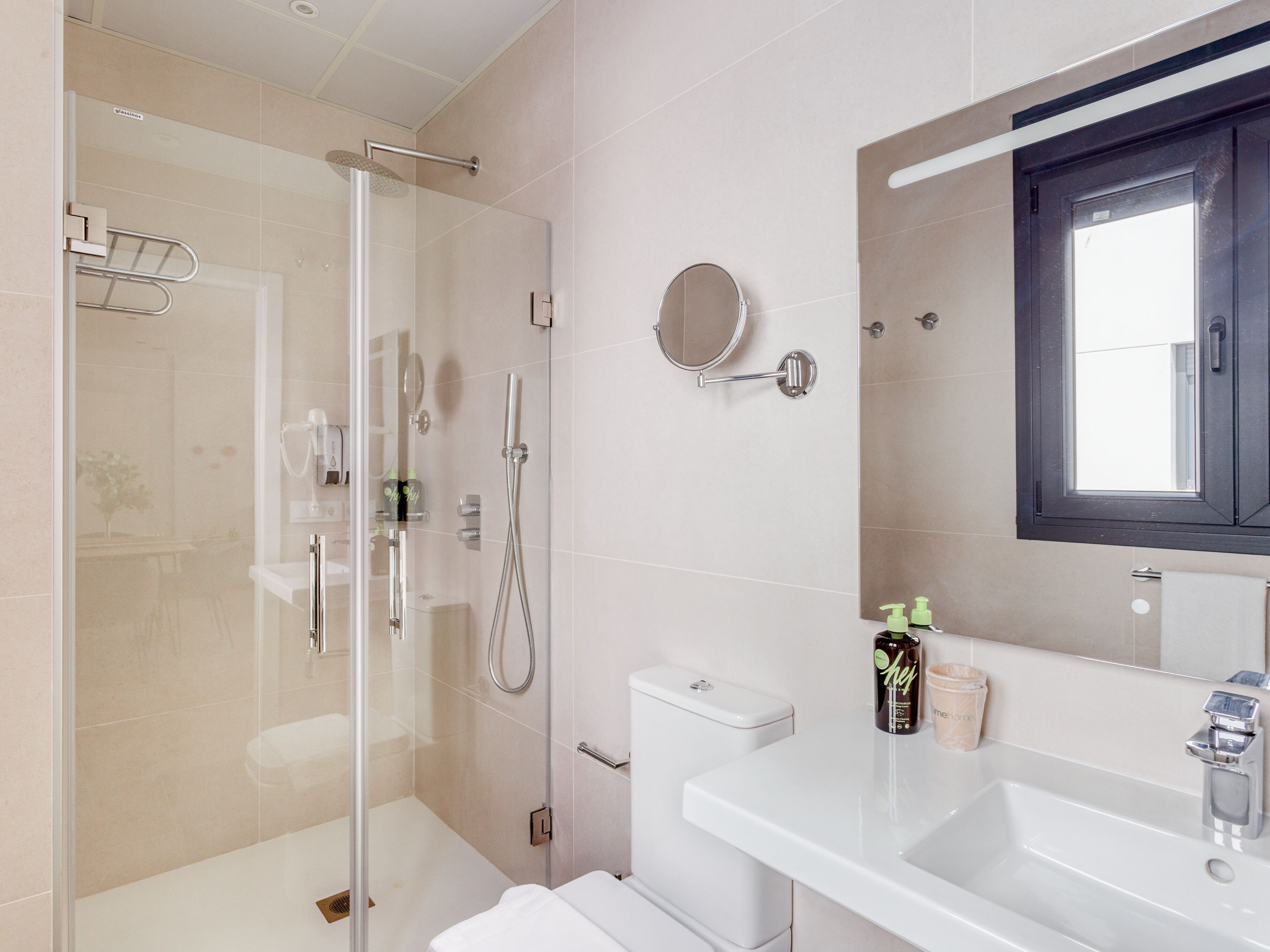 Un baño moderno con cabina de ducha de vidrio, un lavamanos blanco y un espejo sobre él.