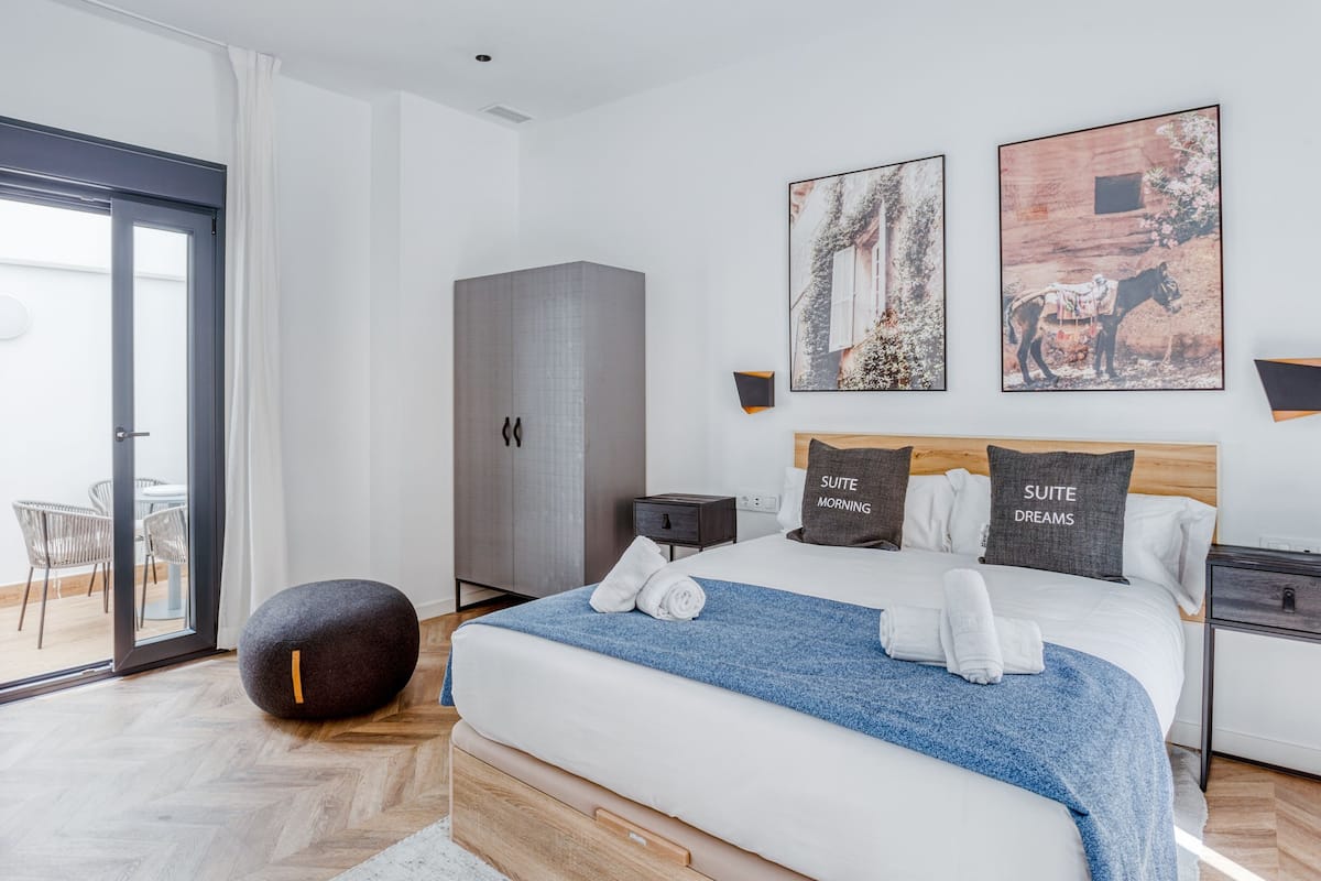 Ein modernes Schlafzimmer mit einem großen Bett, einem Kleiderschrank, einer Sitzecke mit Sesseln und Kunstwerken an den Wänden.