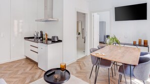 Una cocina moderna con una isla central, un comedor con mesa de madera y sillas grises, y un televisor de pantalla plana montado en la pared.
