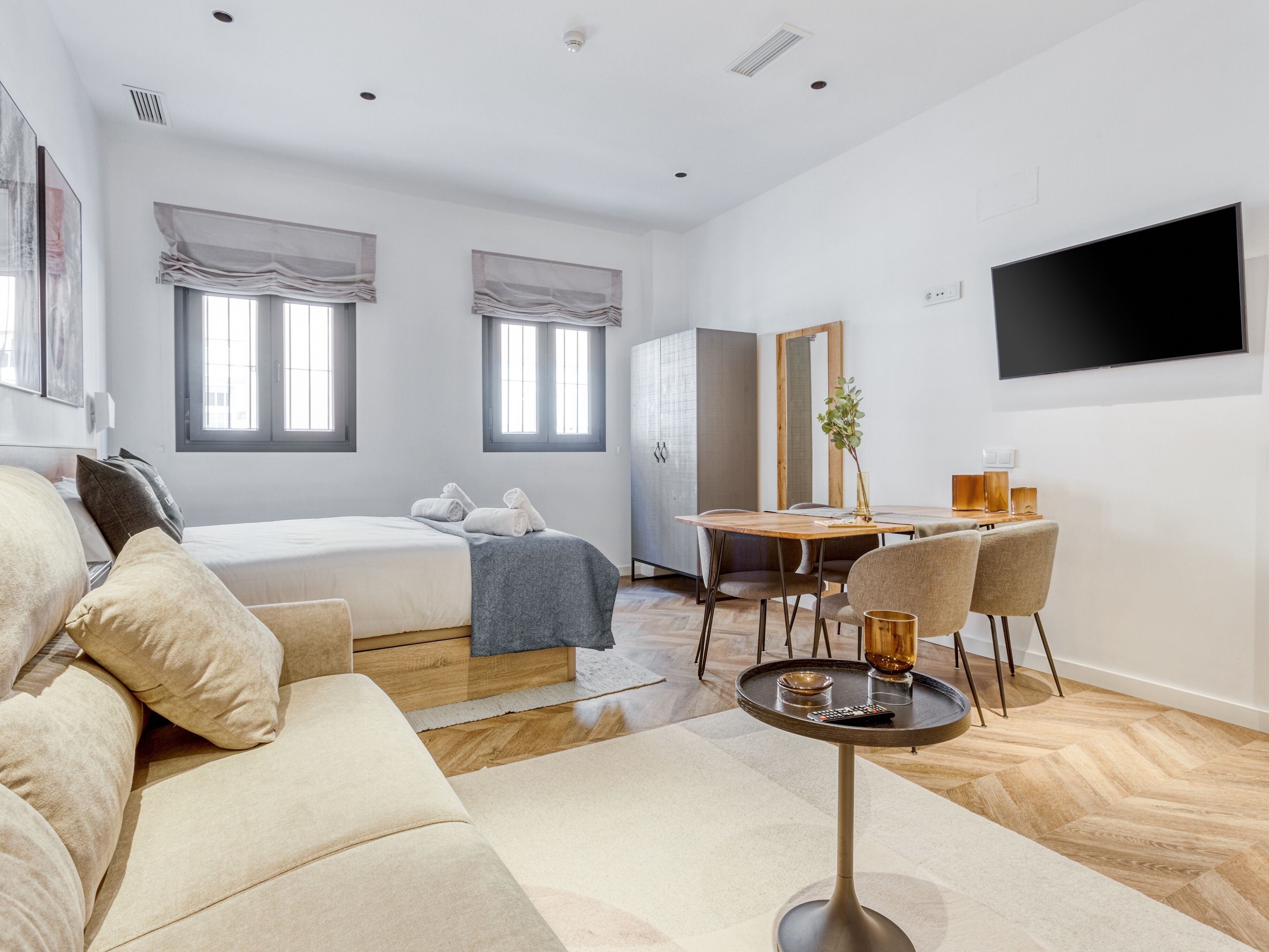 Una habitación de hotel moderna con cama, sofá, mesa de comedor, sillas y televisor.