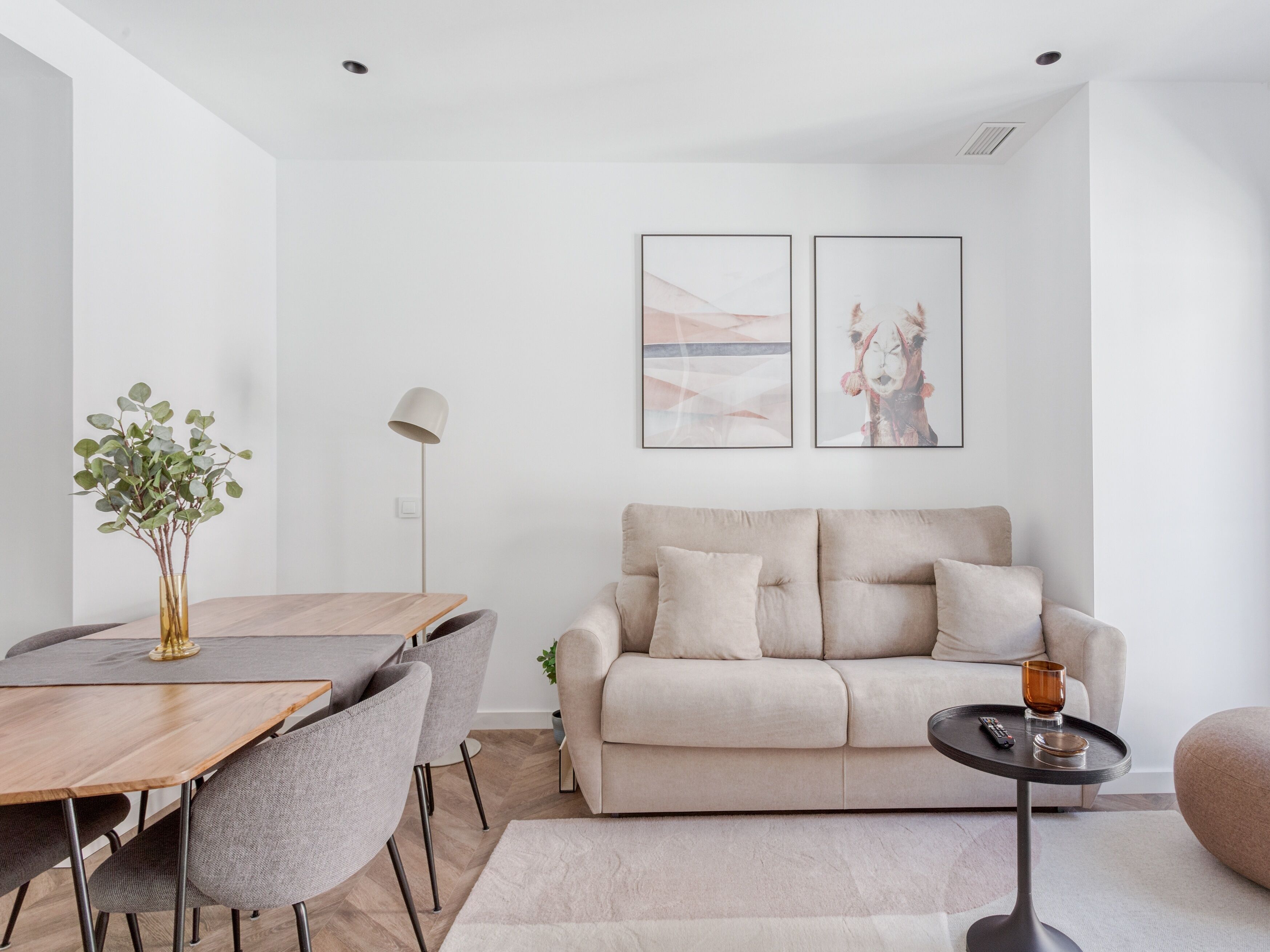 Una sala de estar moderna con un sofá, una mesa de comedor con sillas y dos obras de arte enmarcadas en la pared.