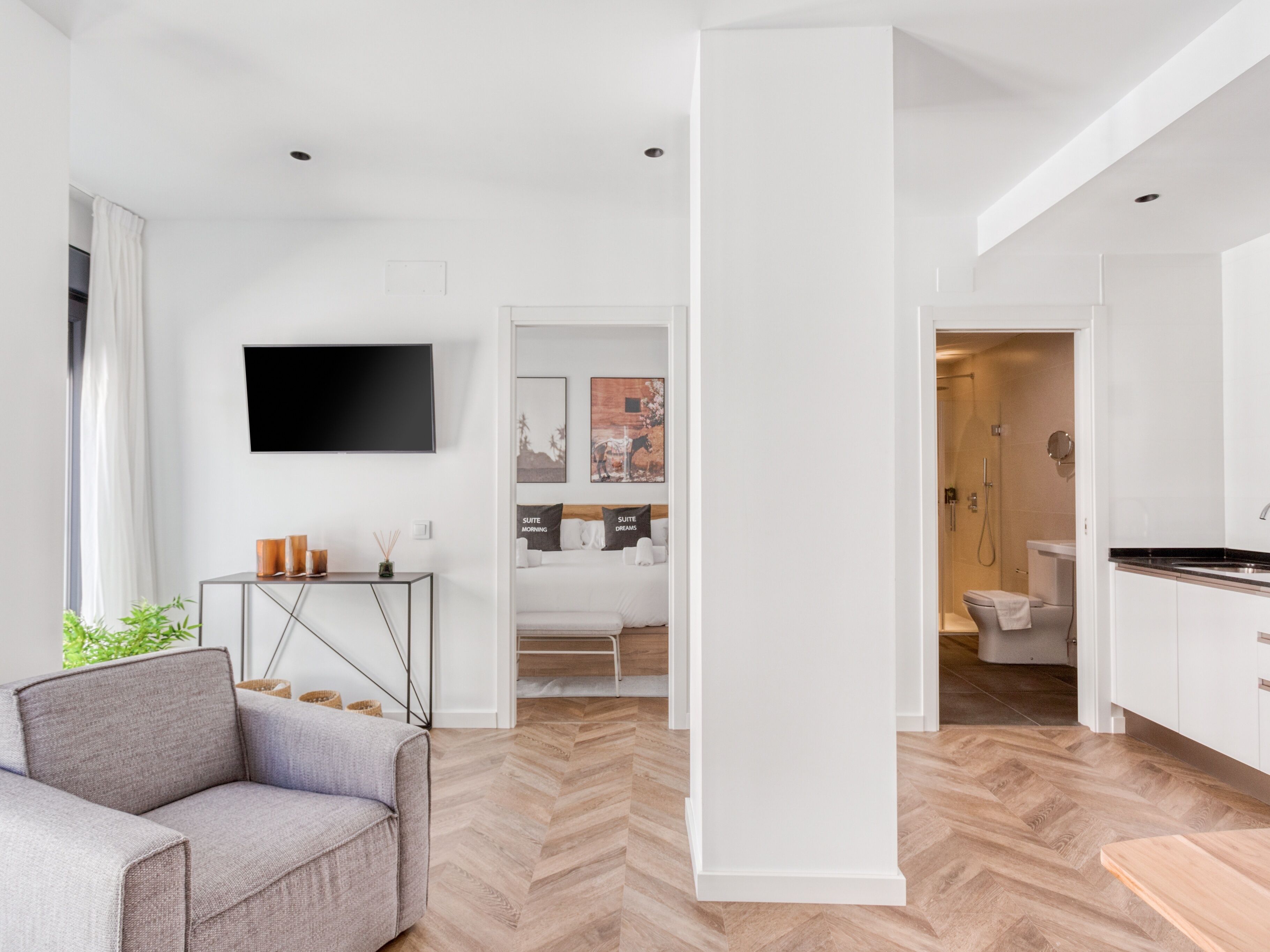Un salon moderne avec un canapé gris, un téléviseur à écran plat et un parquet en bois disposé en chevrons.