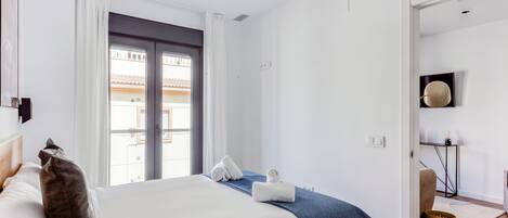 Une chambre moderne avec un grand lit, une fenêtre avec des rideaux, une table de chevet avec une lampe et une vue sur l’extérieur.