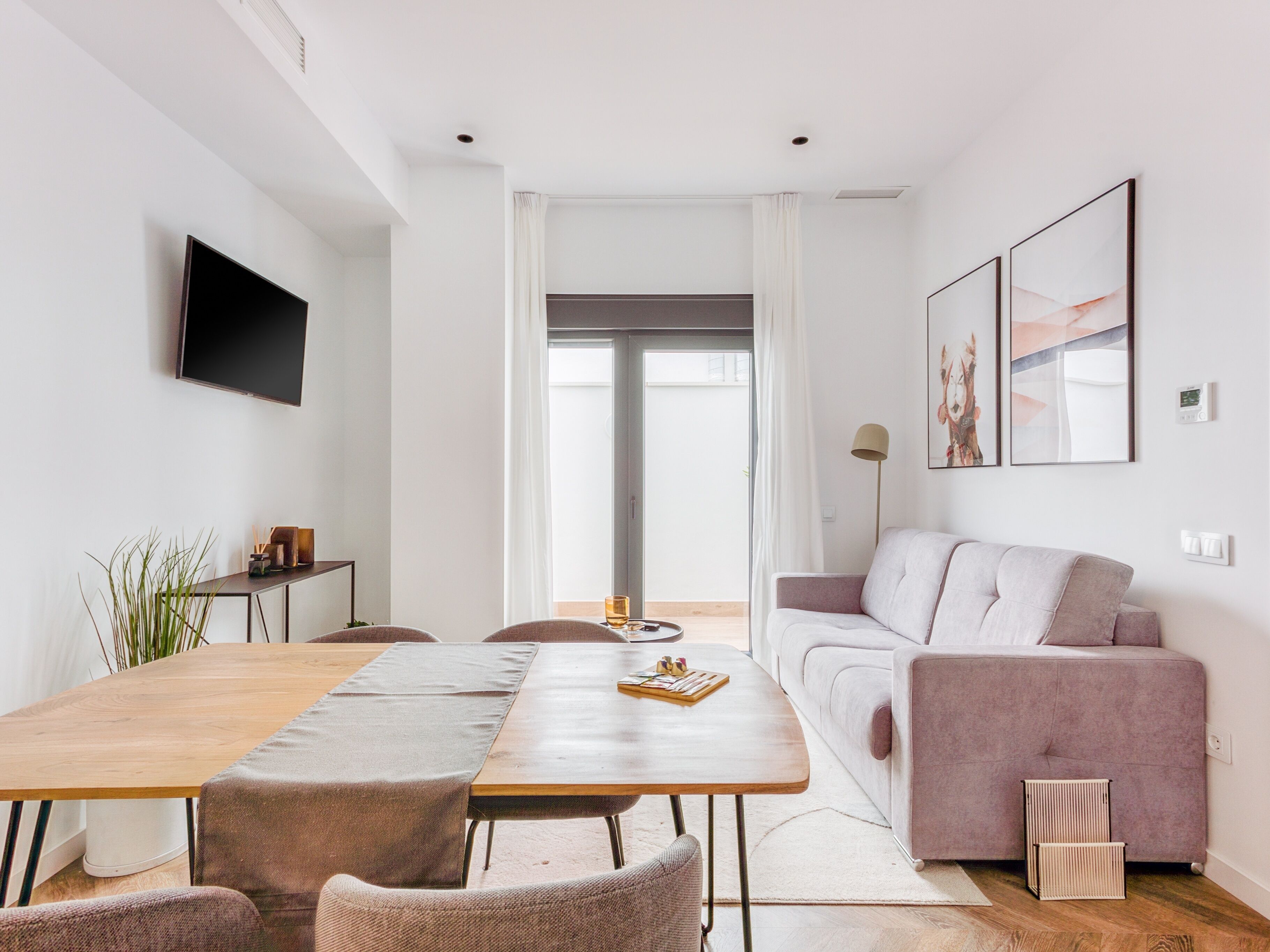 Un salon moderne avec une table à manger en bois, deux chaises, un canapé et un téléviseur fixé au mur.