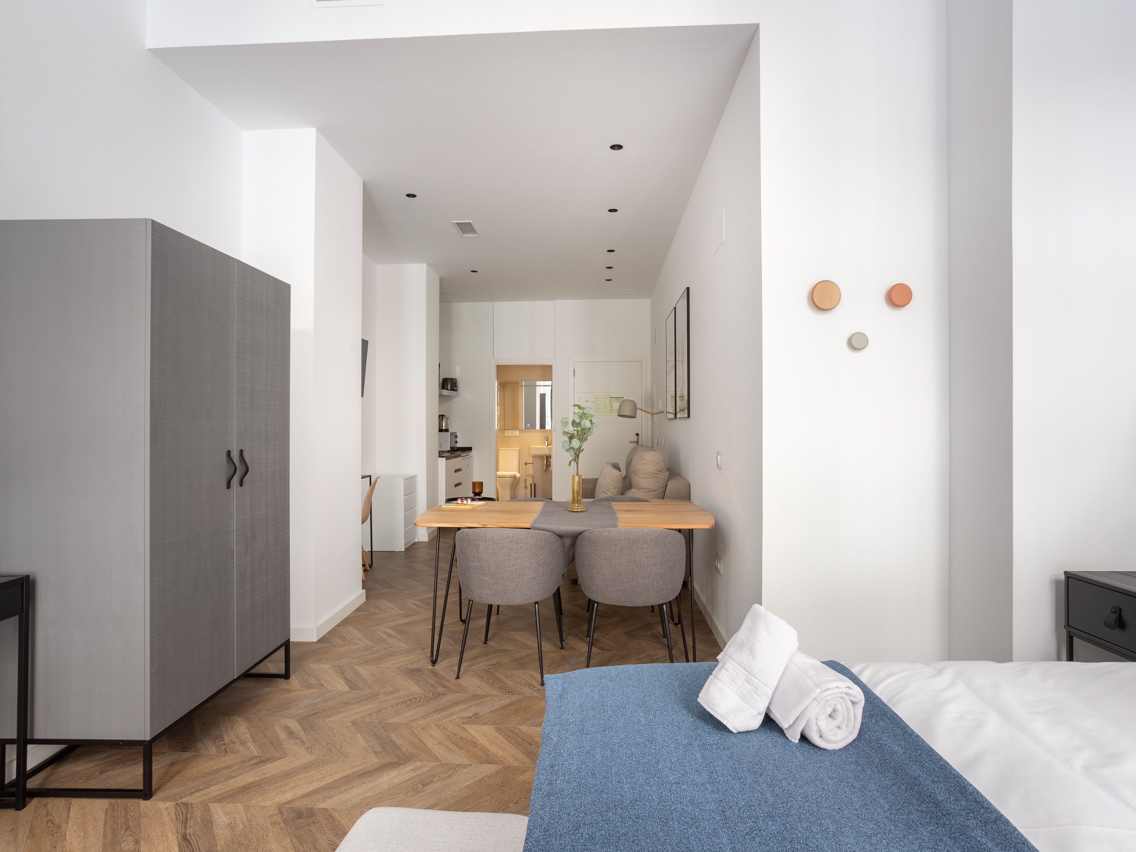 A modern hotel room with a bed, a desk, and a kitchenette.