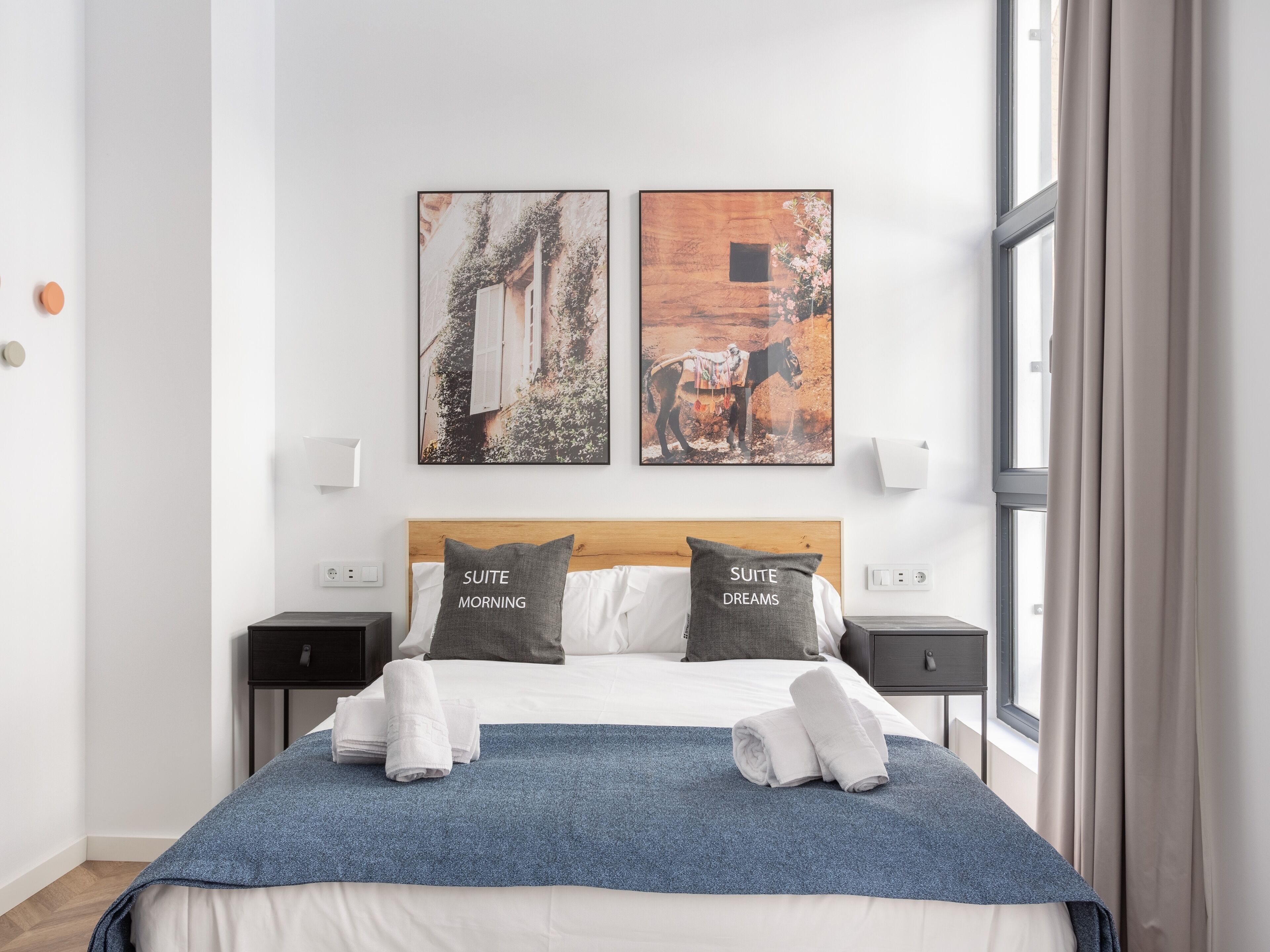 Una habitación de hotel con una cama, dos almohadas, un edredón azul y dos obras de arte en la pared.