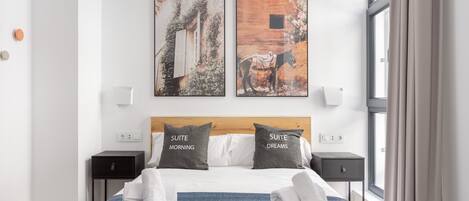 A hotel room with a bed, two pillows, a blue blanket, and two artworks on the wall.