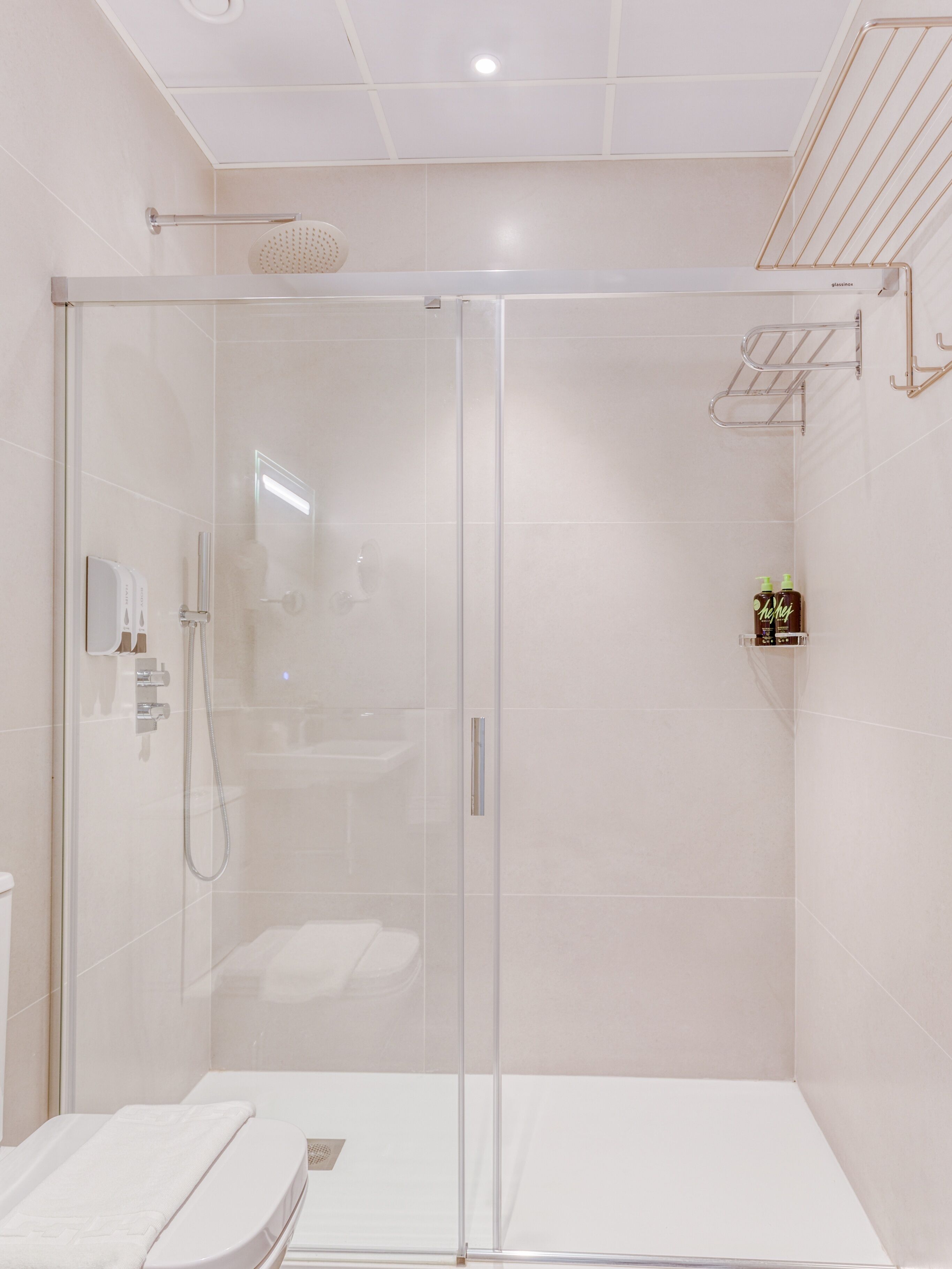 A modern bathroom with a glass-enclosed shower, a white sink, and a towel rack.