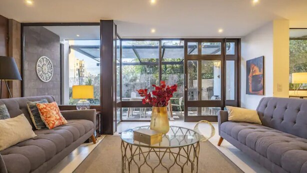 Una sala de estar moderna con dos sofás, una mesa de centro de cristal y un ventanal con vistas al exterior.