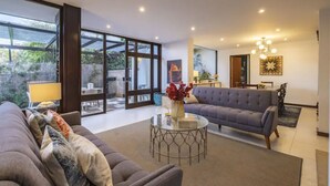 Una sala de estar moderna con un sofá, una mesa de centro de vidrio y un comedor con candelabro.