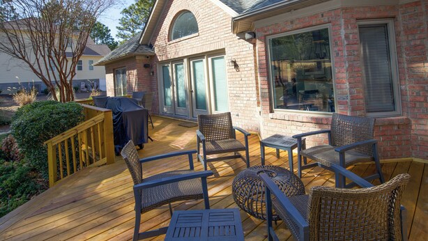 En terrasse med fletmøbler, grill og et murstenshus med store vinduer.
