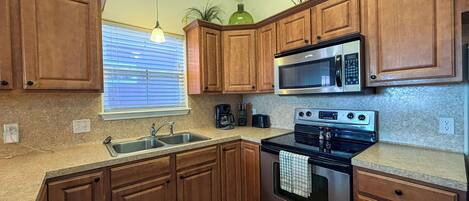 A kitchen with wooden cabinets, a stainless steel microwave, a stove, and a sink.