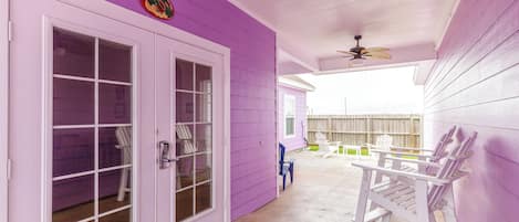 A covered porch with a purple exterior, white doors, and a ceiling fan.