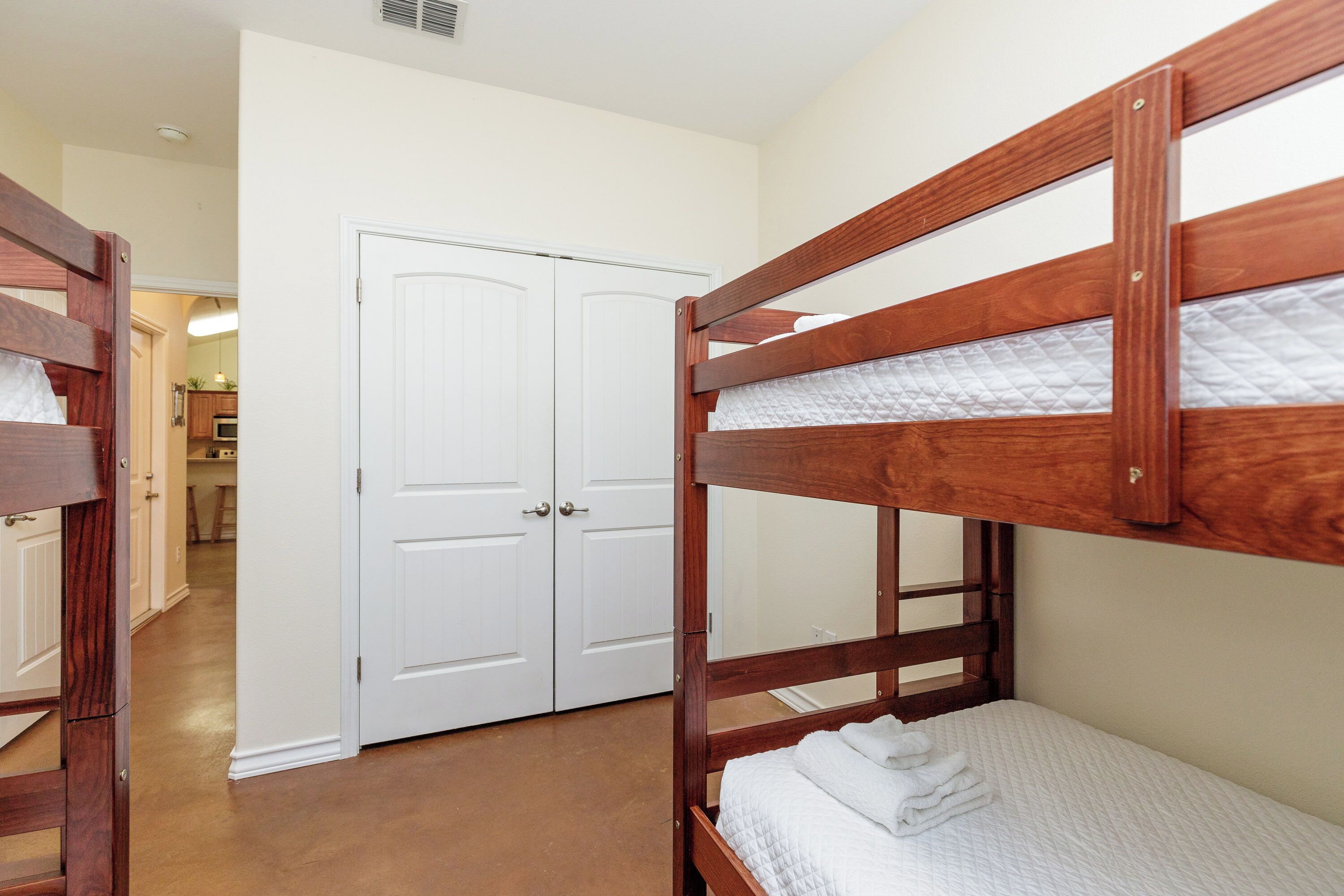 A bedroom with two bunk beds, a white door, and a hallway leading to a kitchen area.