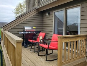 Een terras met een barbecue en rode stoelen.