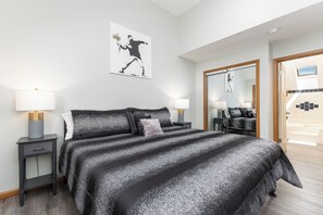 Een moderne hotelkamer met een groot bed, twee nachtkastjes met lampen, een spiegel en een deur naar een badkamer.