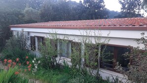 Ein Haus mit rotem Ziegeldach, umgeben von üppigem Grün und blühenden Pflanzen.