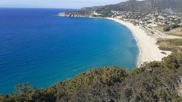 Eine Küstenlandschaft mit blauem Meer, Sandstrand und hügeliger Kulisse mit Gebäuden.
