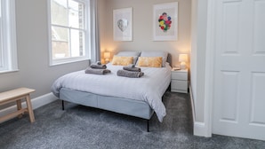 A bedroom with a bed, bedside tables, a bench, and artwork on the walls.