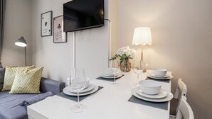 A modern dining area with a flat-screen TV mounted on the wall, a table set for dining with plates, glasses, and a vase of flowers.