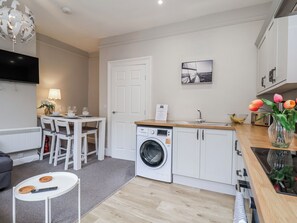 A compact kitchen with a washing machine, a dining area with chairs, a table, and a TV.