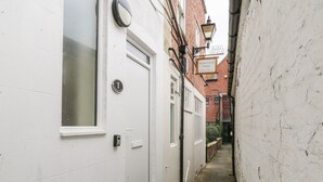 A narrow alleyway with white-painted walls, a door with a number plate, and a street lamp.