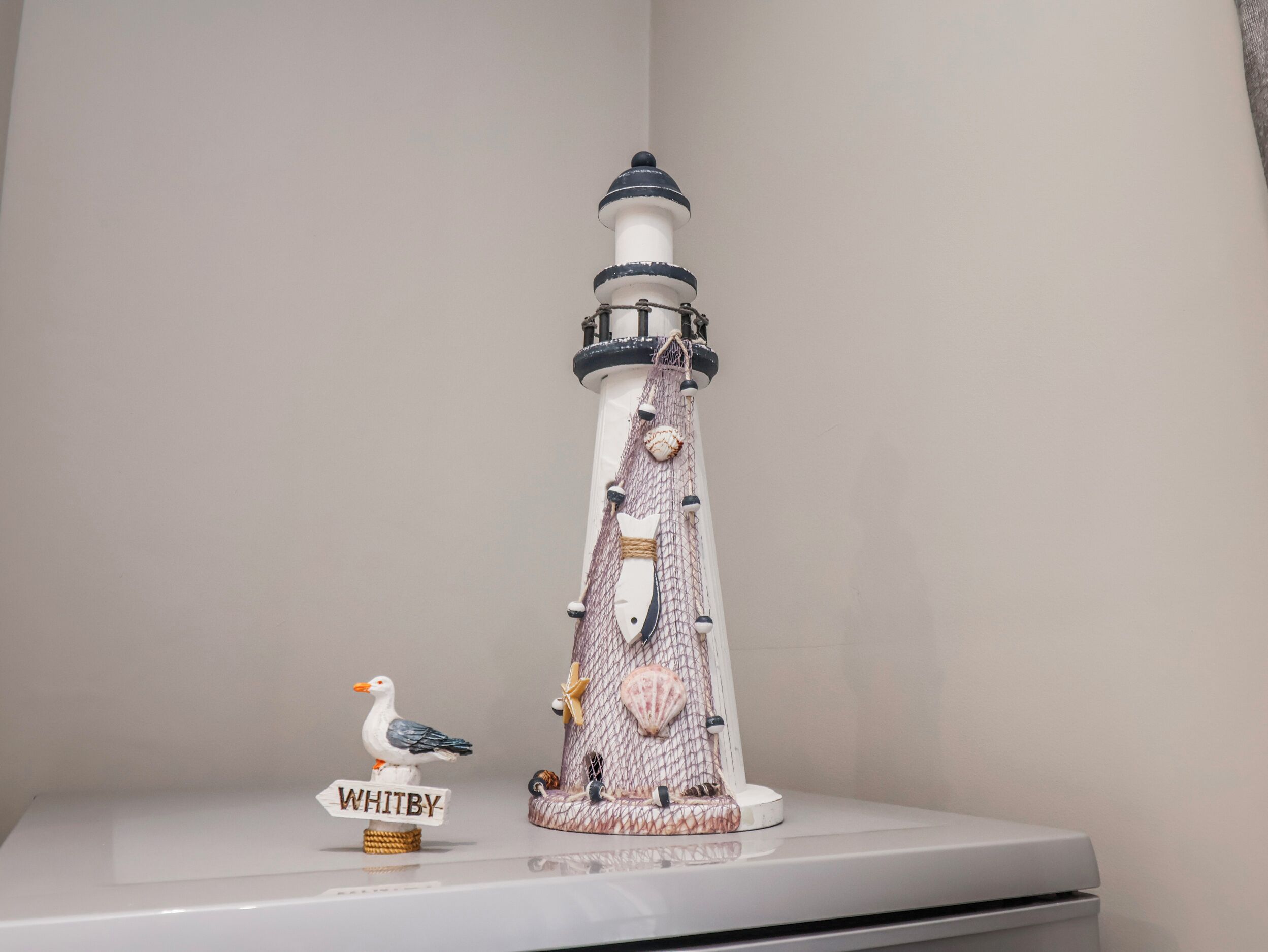 Een witte plank met een model van een vuurtoren en een zeemeeuwbeeldje.
