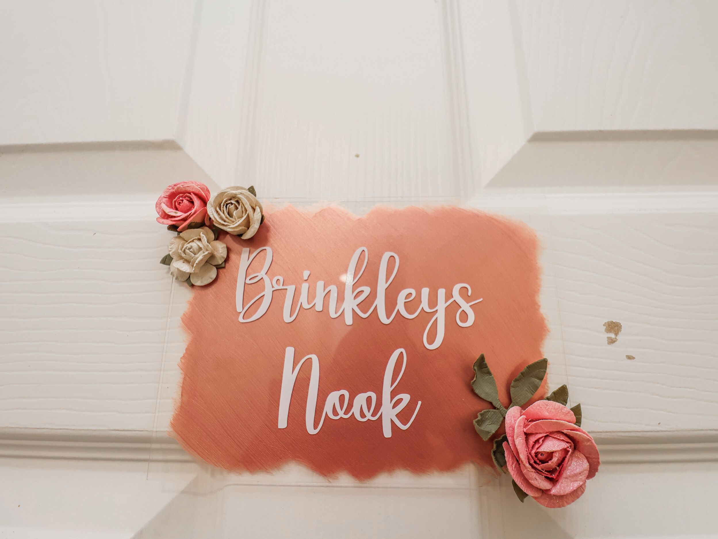 Une pancarte portant l’inscription « Brinkleys Nook », entourée de fleurs décoratives.