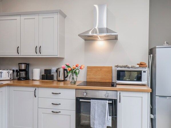 A modern kitchen with white cabinets, a stainless steel range hood, a toaster, a coffee maker, a microwave, and a small oven.