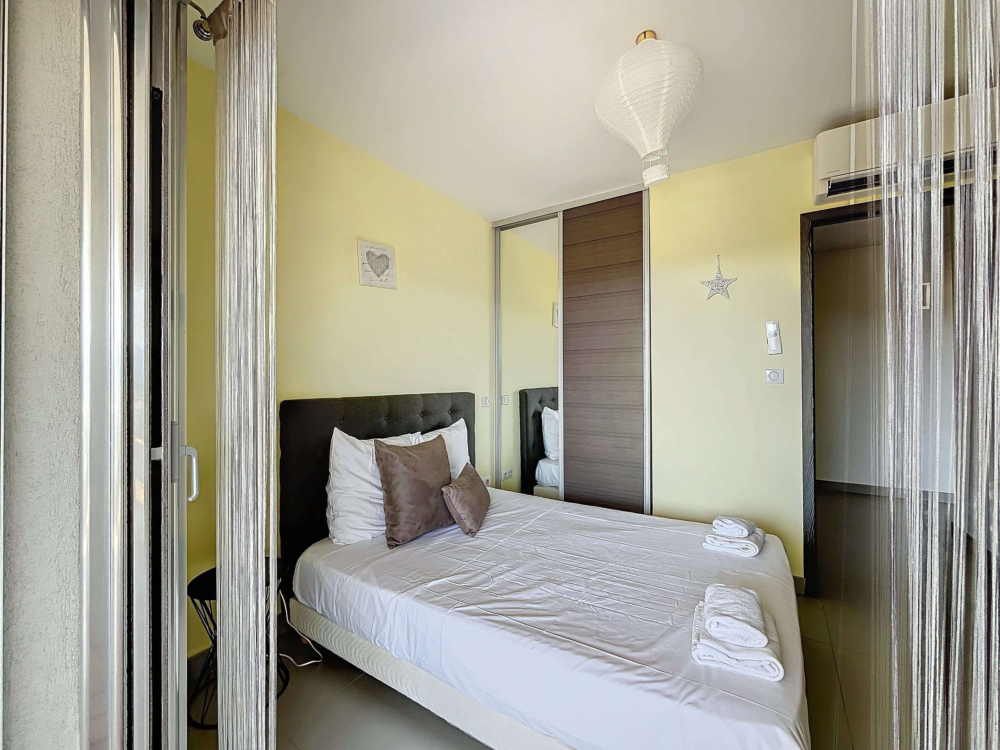 Una cama bien hecha con sábanas blancas y un cojín marrón, una mesita de noche, un aire acondicionado de pared y una decoración con forma de estrella.