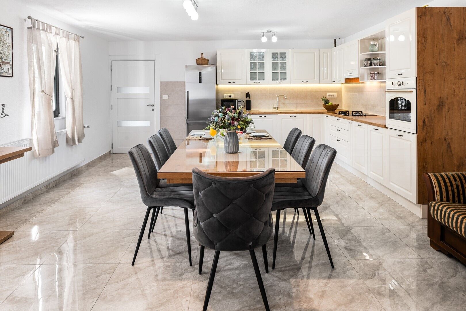 A modern kitchen with white cabinets, a central island, and a dining area with a glass-top table and chairs.