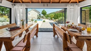 Een eetgedeelte met houten banken en tafels, een schaakbord, en uitzicht op een zwembad en tuin.