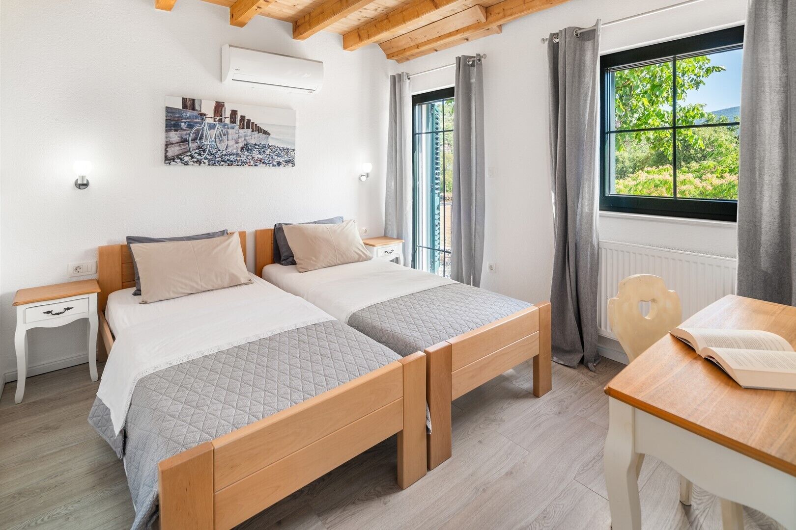 A bedroom with two beds, a wooden ceiling, a window with curtains, a radiator, and a wall-mounted air conditioner.