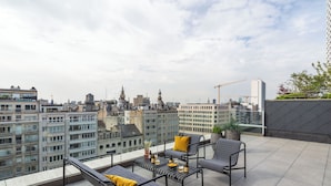 Terraza en la azotea con asientos al aire libre, una planta en maceta y vista panorámica de la ciudad.