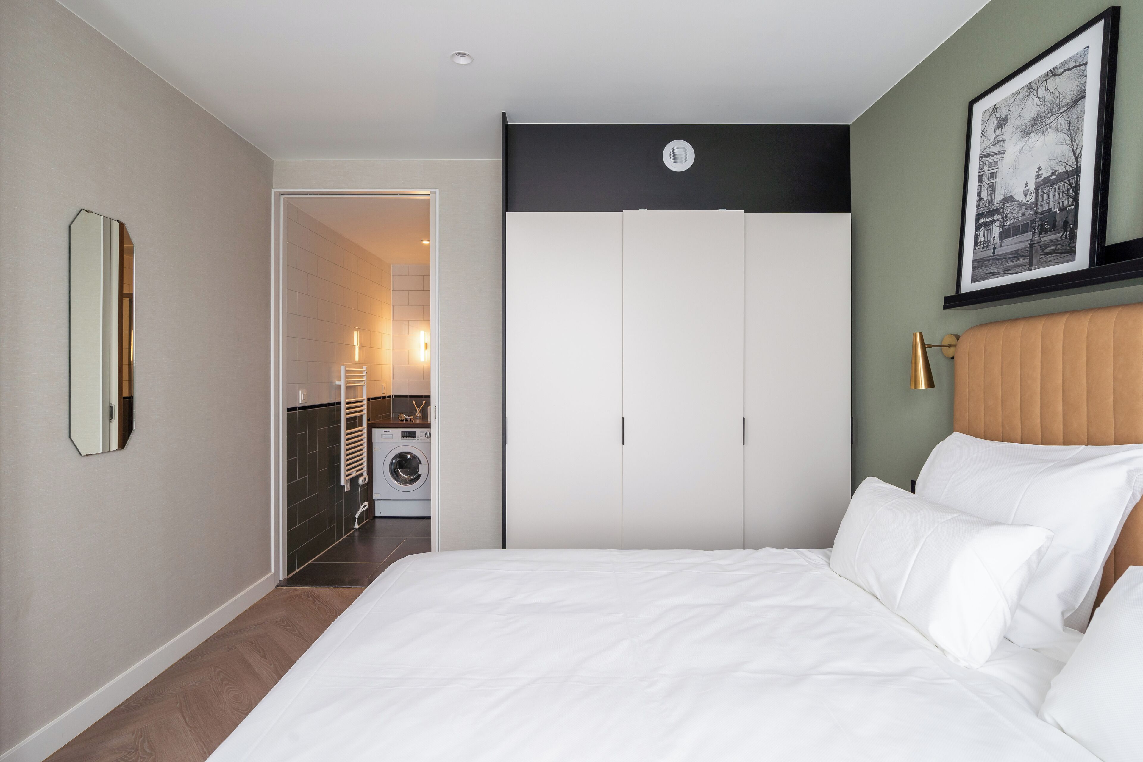A bedroom with a large bed, a wardrobe, a mirror, and a framed picture on the wall.
