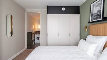 Een slaapkamer met een groot bed, een kledingkast, een spiegel en een lijst met een afbeelding aan de muur.