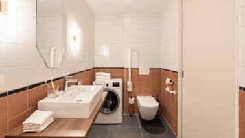 A modern bathroom with a sink, washing machine, toilet, and a mirror.