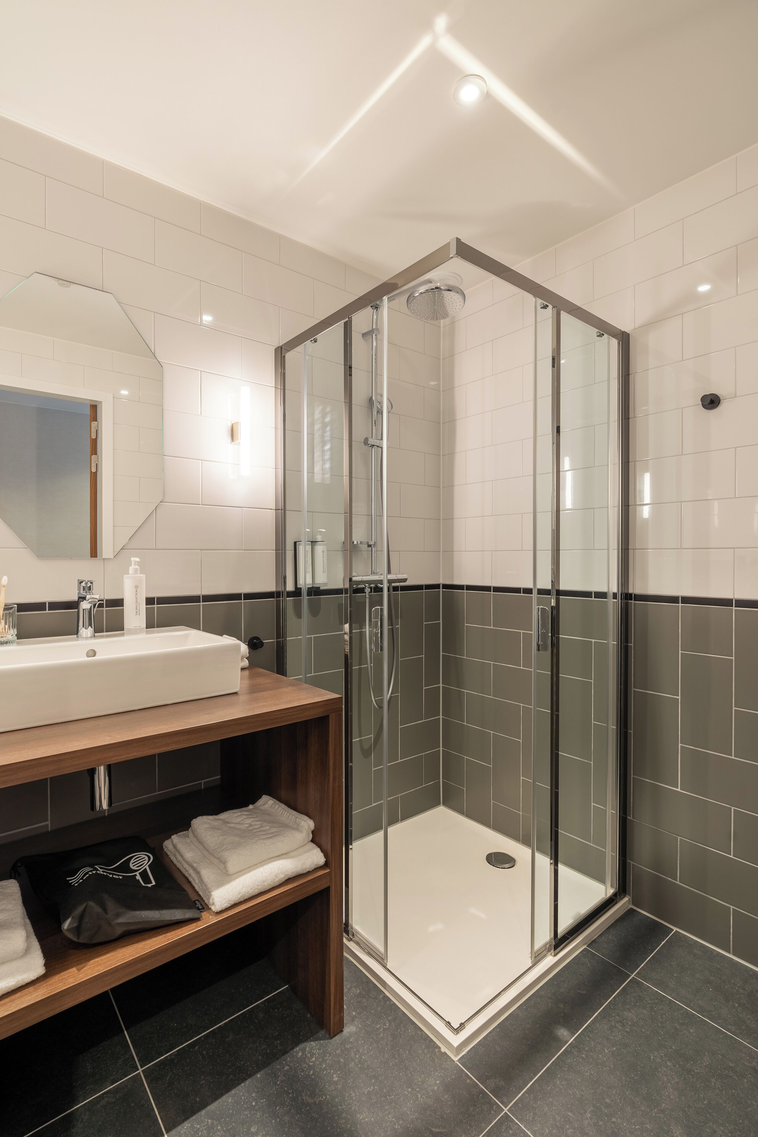 Een moderne badkamer met een douchecabine van glas, een grote spiegel en een houten wastafelmeubel met handdoeken.