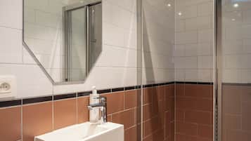 A modern bathroom with a white sink, a glass shower enclosure, and a mirror on the wall.