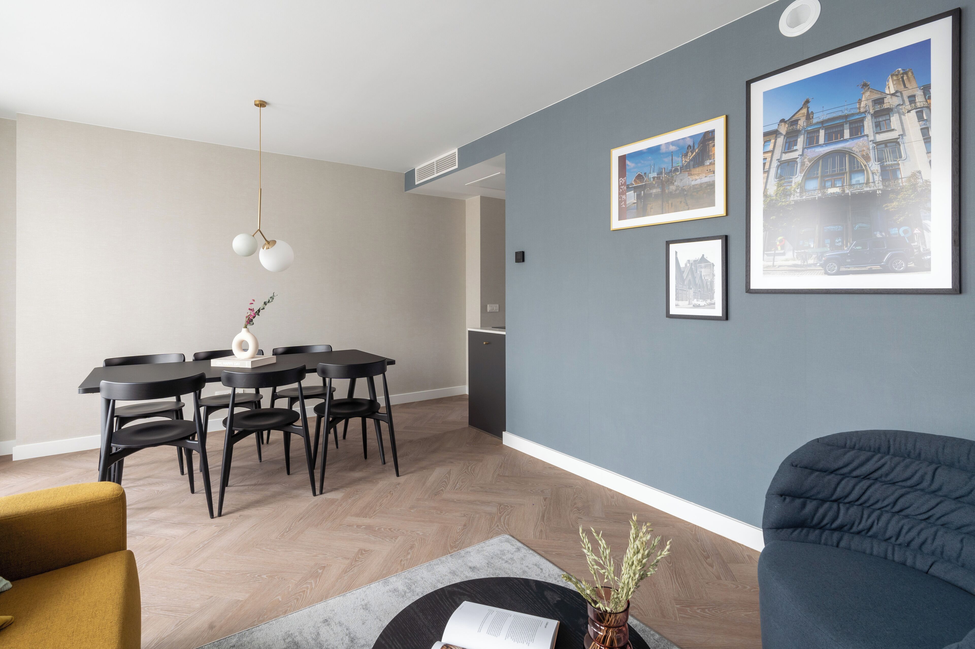 Ein modernes Wohnzimmer mit Essbereich, mit einer hellblauen Wand, Holzboden und einem dunkelblauen Sofa.