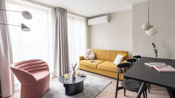Una sala de estar moderna con un sillón rosa, un sofá amarillo, una mesa de centro redonda y una mesa de comedor con sillas.