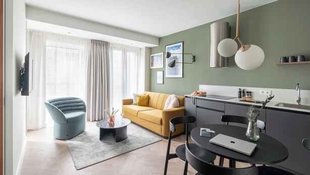 Una sala moderna con un sofá, una mesa de comedor con sillas, un televisor de pantalla plana y una zona de cocina con un fregadero y una encimera.